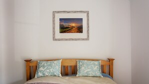 Een slaapkamer met een houten hoofdbord, een bed met een gestreept laken en een lijst met een landschapsfoto aan de muur.