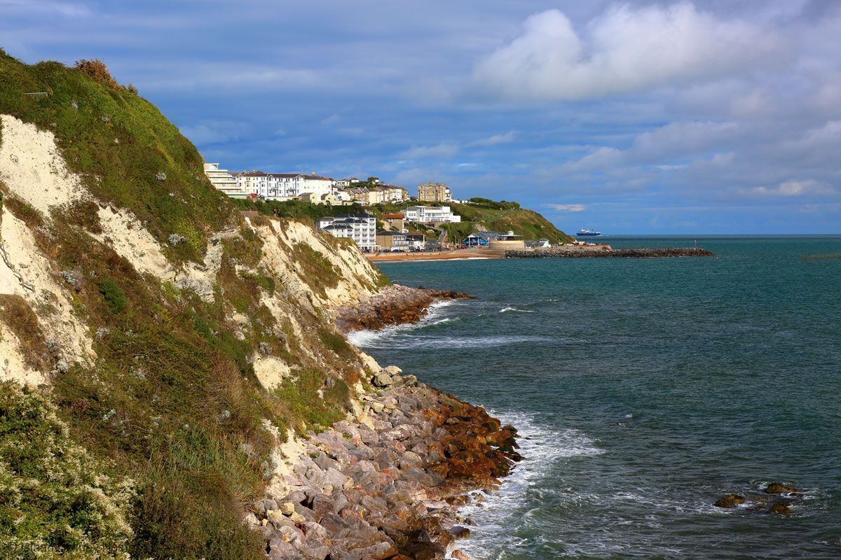 A coastal area with buildings on a hillside, a rocky shoreline, and calm sea.