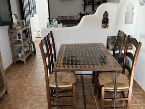 A dining area with a square table and six chairs, a tiled floor, and a white wall with a window. - House with terrace and great views (Albuñuelas)
