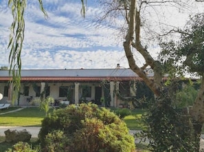 A building with a red-tiled roof, a covered patio area, and a well-maintained garden with various plants and a large tree.