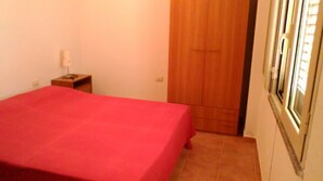 Ein Schlafzimmer mit roter Bettdecke, einem Holzschrank und einem kleinen Nachttisch mit Lampe.