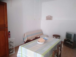 Une petite pièce simple, avec une table, des chaises, un téléviseur et une étagère fixée au mur.