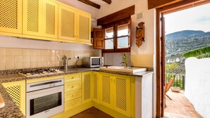 A kitchen with yellow cabinets, a stove, and a microwave. - Cosy restored rural house (Albuñuelas)