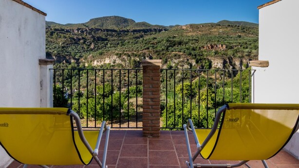 A balcony with yellow chairs, a brick pillar, and a view of a mountainous landscape. - Cosy restored rural house (Albuñuelas)