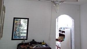 Une pièce avec un ventilateur de plafond, un mur en briques blanches, une commode en bois et un tableau encadré.