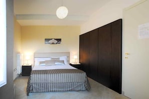Une chambre à coucher avec un lit, des lampes de chevet, une armoire sombre, un tableau encadré au mur et une porte avec une serrure.