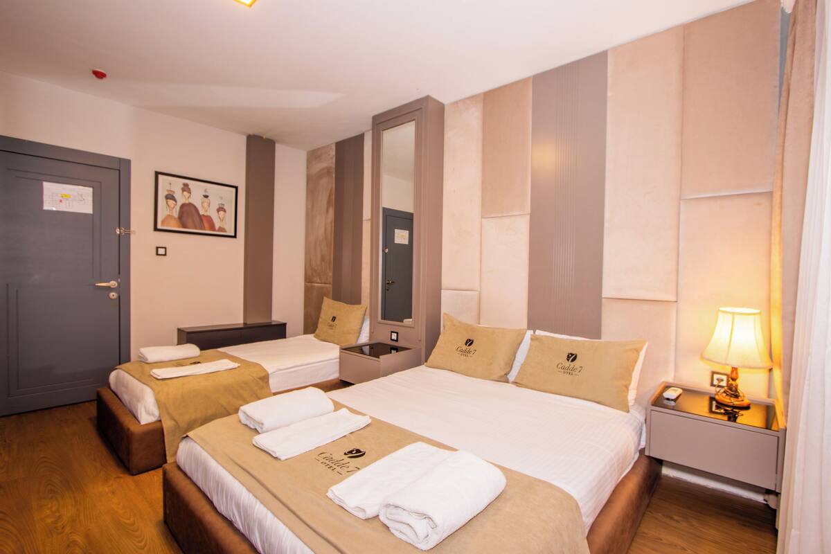 Camera d'albergo con due letti, un comodino, uno specchio e una porta.