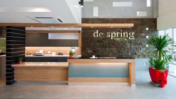 A modern hotel reception area with a stone wall, wooden reception desk, and a large potted plant. - De Spring Hotel (Kuantan)