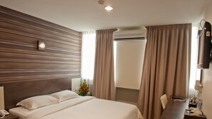 A hotel room with a bed, a bedside telephone, a desk with a chair, a TV, and an air conditioning unit. - De Spring Hotel (Kuantan)