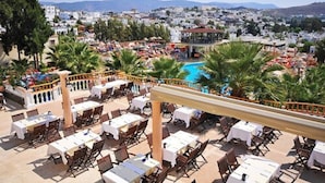 An outdoor dining area with tables and chairs, a pool, and a view of a coastal town. - Phoenix Sun Hotel (Bodrum)