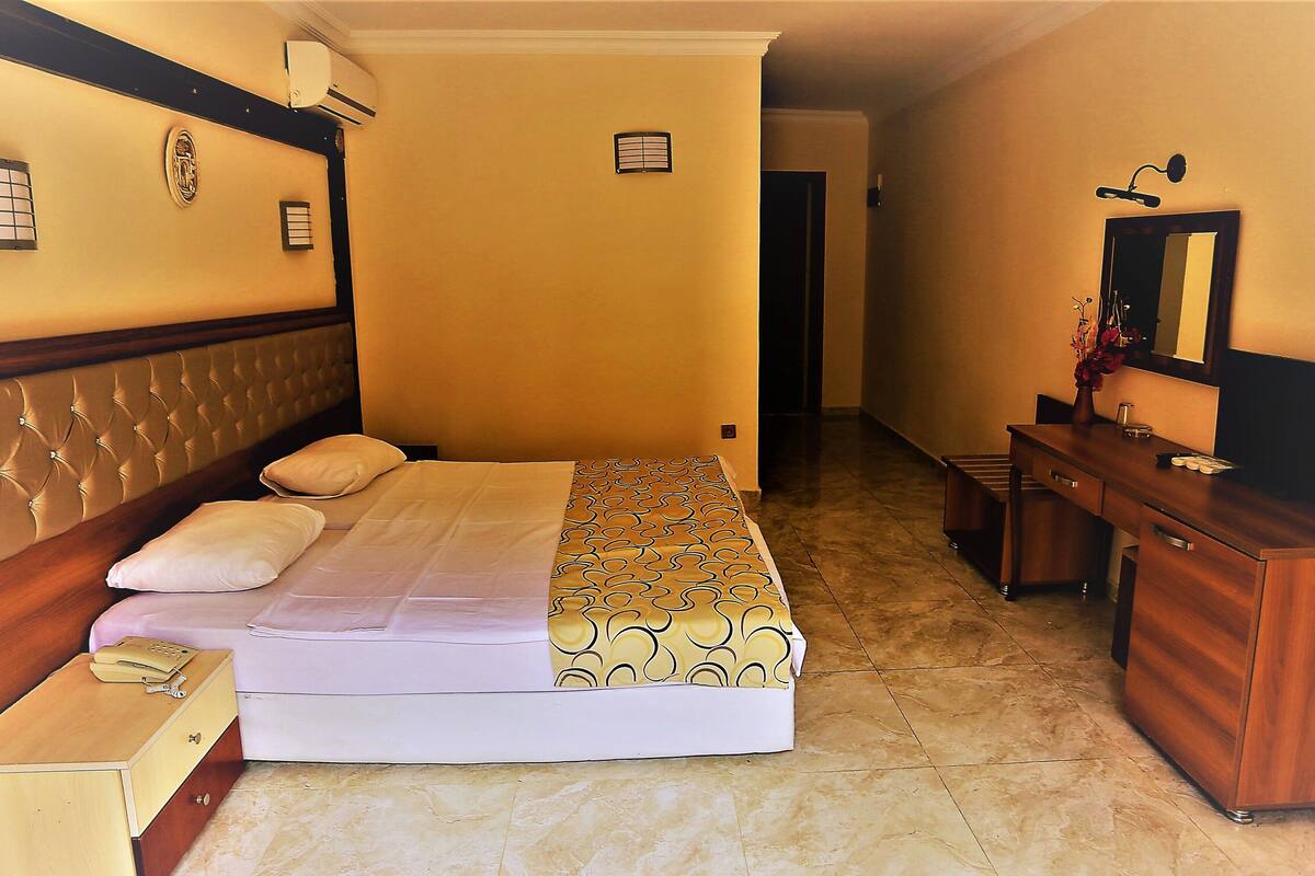 A hotel room with a bed, bedside table, dresser, and a mirror.