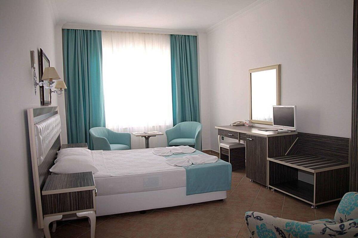A hotel room with a bed, two chairs, a desk, a television, and a mirror.