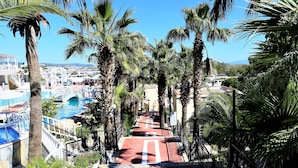 A pathway lined with palm trees leading to a pool area with a clear blue sky above. - Phoenix Sun Hotel (Bodrum)