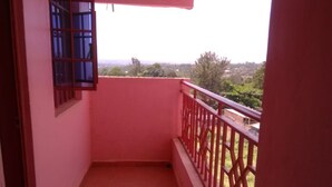 A small balcony with a red railing, a window with bars, and a view of greenery and buildings in the distance. - Veroanto Hotel (Siaya)