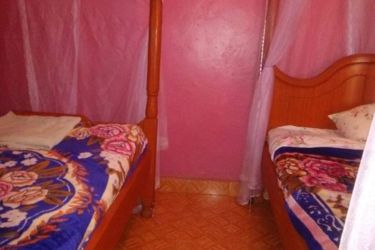 A room with two wooden beds, each with a canopy. The walls are painted pink, and the floor has a herringbone pattern.