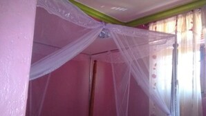 A room with a bed under a canopy, pink walls, and a wooden floor. - Veroanto Hotel (Siaya)