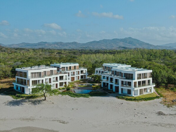 Een modern resort met meerdere gebouwen van twee verdiepingen, een zwembad en een natuurlandschap met bergen op de achtergrond.