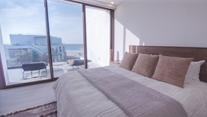 Une chambre avec un grand lit, une vue sur la plage et un balcon avec une chaise.
