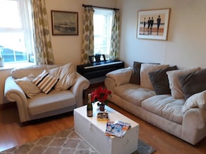 A living room with two sofas, a coffee table with magazines, a piano, and a window with curtains.