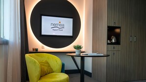 A modern hotel lobby with a yellow armchair, a small table with a plant, and a large screen displaying the hotel name.