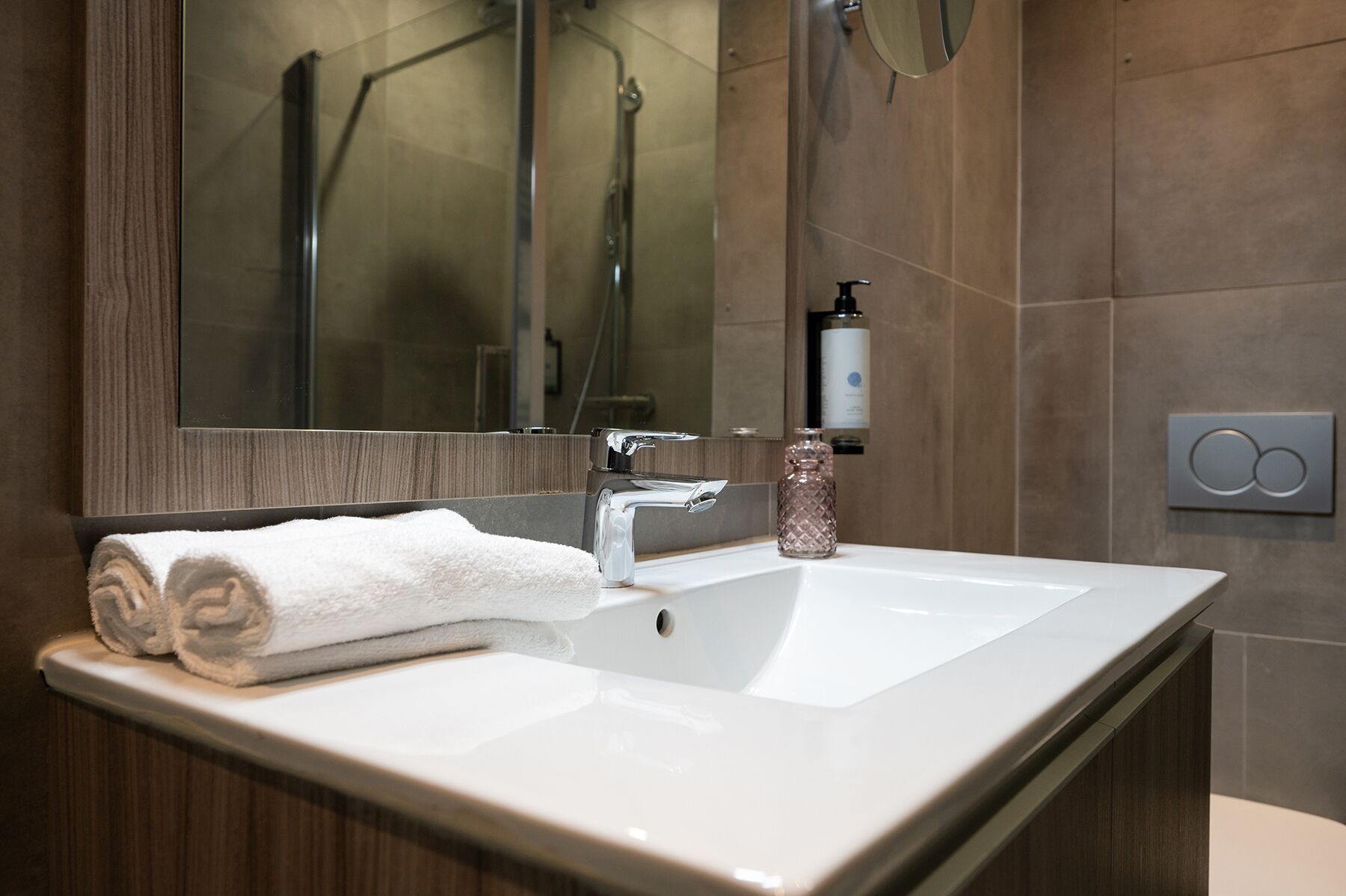 A modern bathroom with a white sink, a glass shower enclosure, and a large mirror.