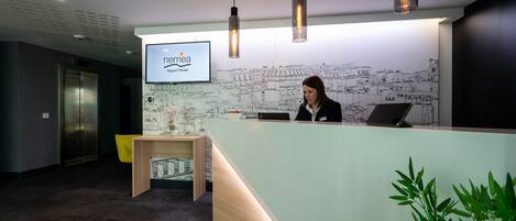 A reception desk with a cityscape mural, a laptop, and a plant.