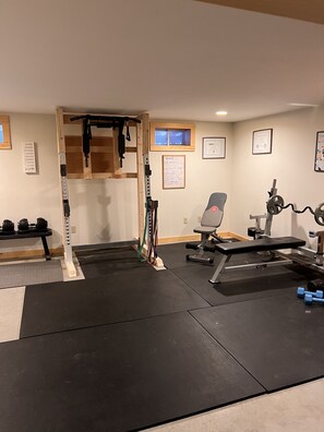 Une salle de sport à domicile équipée d’une barre de traction, d’un banc de musculation, d’haltères et d’un appareil à développé couché.