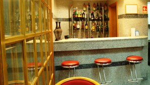 A bar area with a granite countertop, multiple liquor bottles, and red bar stools. - Residencial Horizonte (Lisbon)