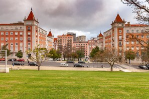 A cityscape with historic buildings featuring red roofs and white facades, a green park in the foreground, and a busy street with cars and pedestrians. - Residencial Horizonte (Lisbon)