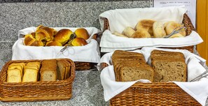 Three wicker baskets containing various breads and rolls, placed on a granite countertop. - Residencial Horizonte (Lisbon)