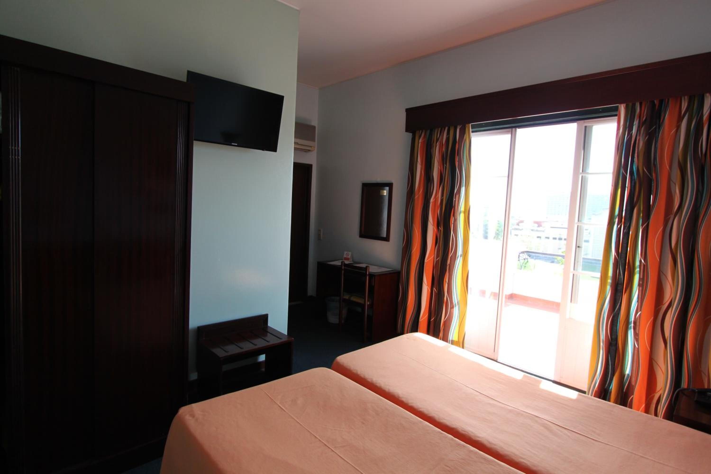 Habitación de hotel con cama, escritorio, silla, televisor y ventana con cortinas.