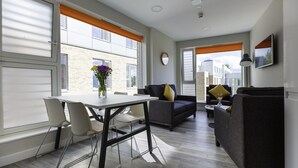 A modern living room with a dining area, large windows, and a view of the cityscape. - The Westwood Apartments (Galway)