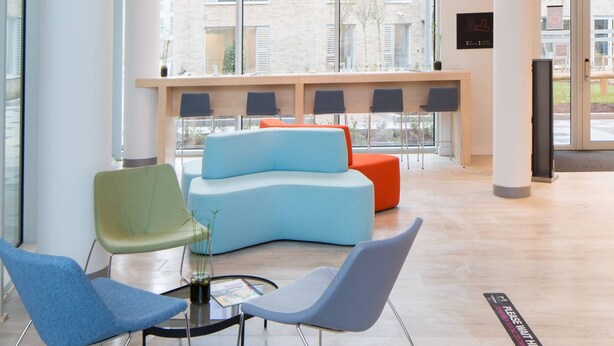 A spacious lobby with a modern blue sofa, green and blue chairs, and a wooden reception desk. - The Westwood Apartments (Galway)