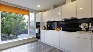 A modern kitchen with white cabinets, a black stove, and a view of trees through a large window. - The Westwood Apartments (Galway)