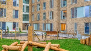 A modern building with multiple floors, large windows, and a grassy courtyard with wooden structures. - The Westwood Apartments (Galway)
