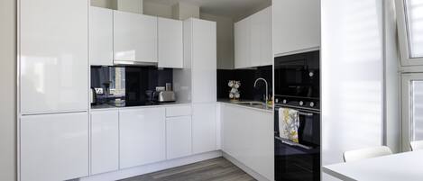 A modern kitchen with white cabinets, a black oven, and a white dining table.