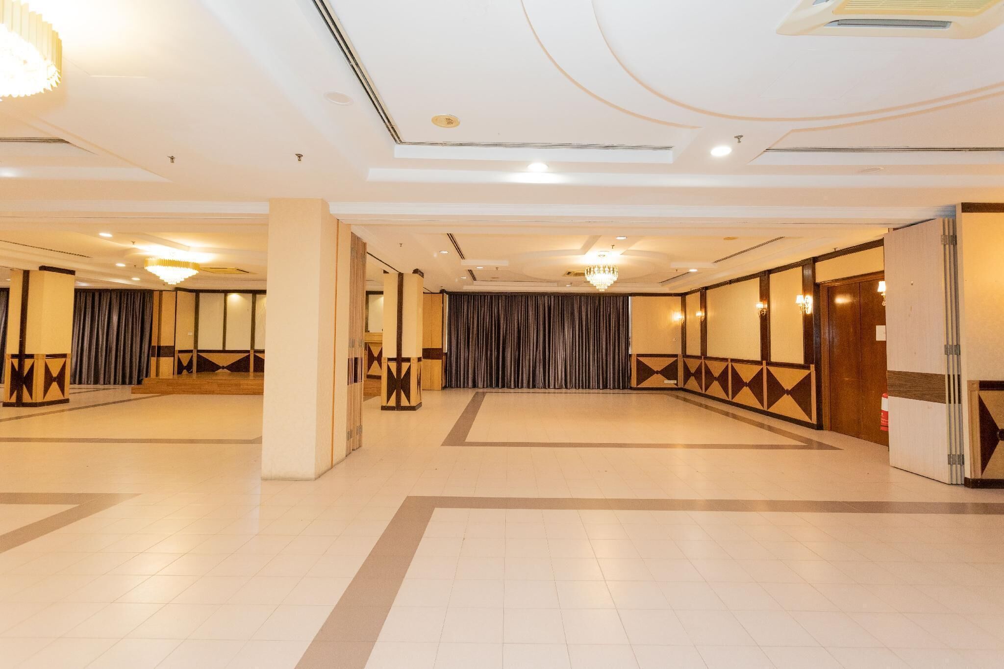 A spacious hotel lobby with a high ceiling, chandeliers, and a large curtain wall.