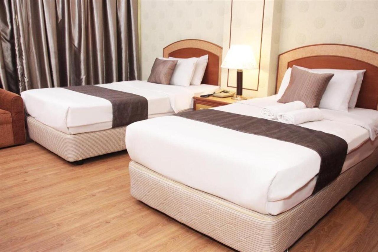Ein Hotelzimmer mit zwei Einzelbetten, Holzboden, Vorhang, Nachttisch mit Lampe und Telefon.