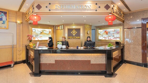 A hotel reception desk with a 'PELICAN' logo, a 'RECEPTION' sign above, and two red lanterns. - Pelican Hotel (Batu Pahat)