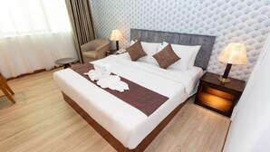 A hotel room with a bed, two bedside tables, a chair, a small round table, and a patterned wall. - Pelican Hotel (Batu Pahat)