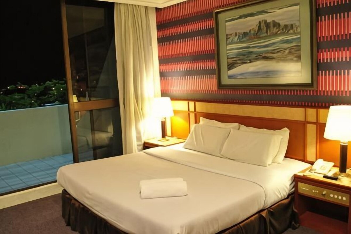 A hotel room with a large bed, two bedside lamps, a nightstand, a painting on the wall, and a view of the outdoors.