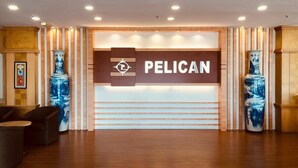 A reception area with a sign reading 'PELICAN,' wooden paneling, and two large vases. - Pelican Hotel (Batu Pahat)