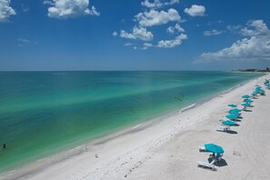 Een strand met helder turquoise water, wit zand en rijen blauwe parasols.