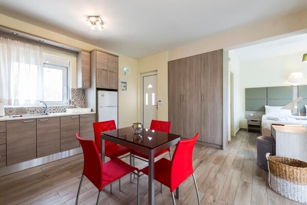 Una cocina compacta con electrodomésticos modernos, un comedor con sillas rojas y un dormitorio con cama y mesita de noche.