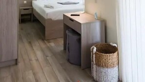 Hotellihuone, jossa on sänky, yöpöytä, lamppu, peili ja pieni roskakori.