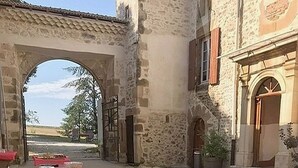 An outdoor dining area with tables covered in red tablecloths, set up in a courtyard with stone buildings and an archway.