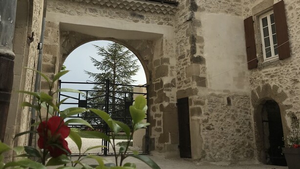 A courtyard with a stone building featuring an archway and a tower.