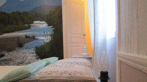 A bedroom with a bed, a nightstand, a lamp, a decorative wall mural, and a window with curtains.