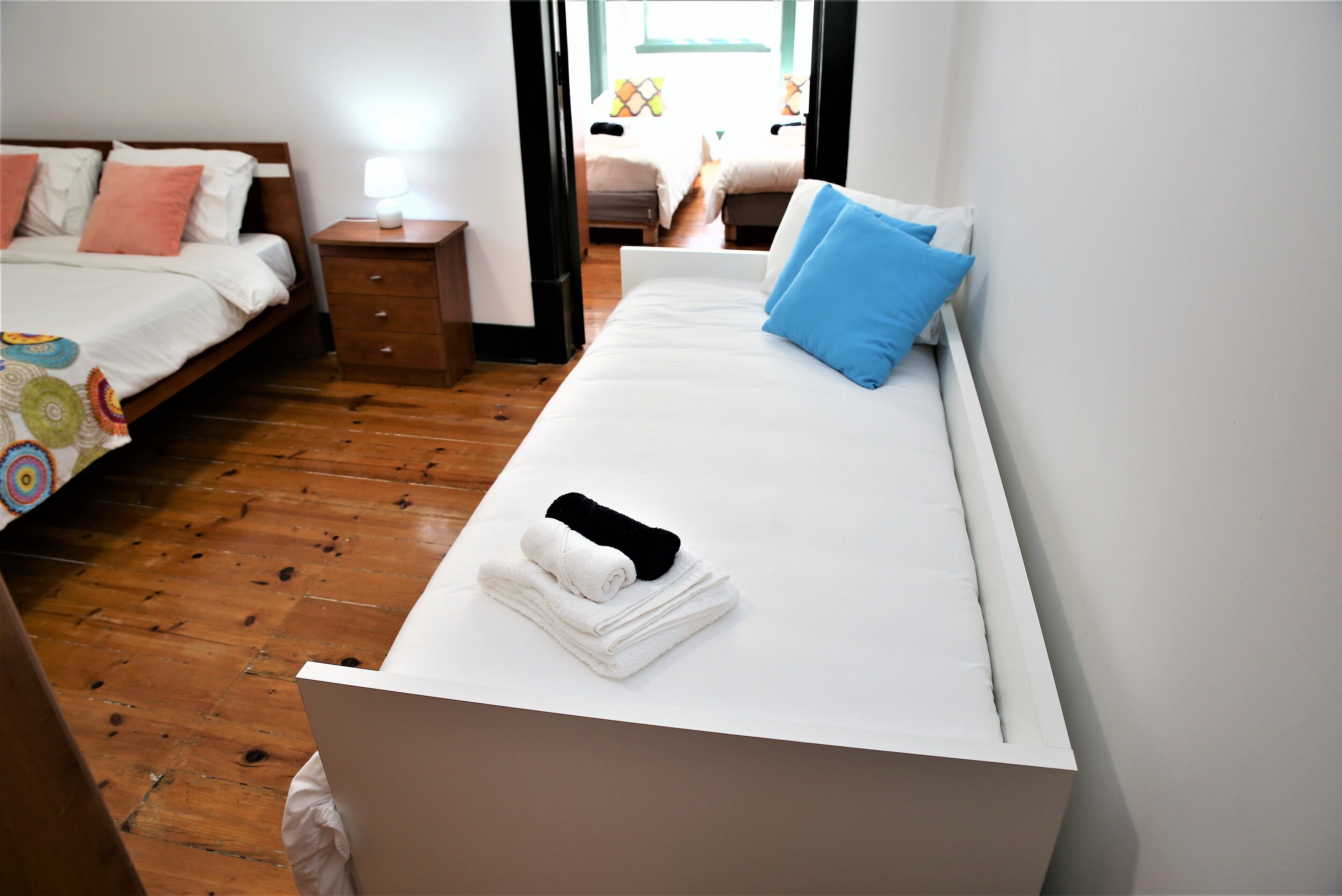 Een hotelkamer met een eenpersoonsbed, nachtkastje en uitzicht op een andere kamer.