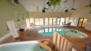 Piscina interior com duas banheiras de hidromassagem, deck de madeira e ventiladores de teto.